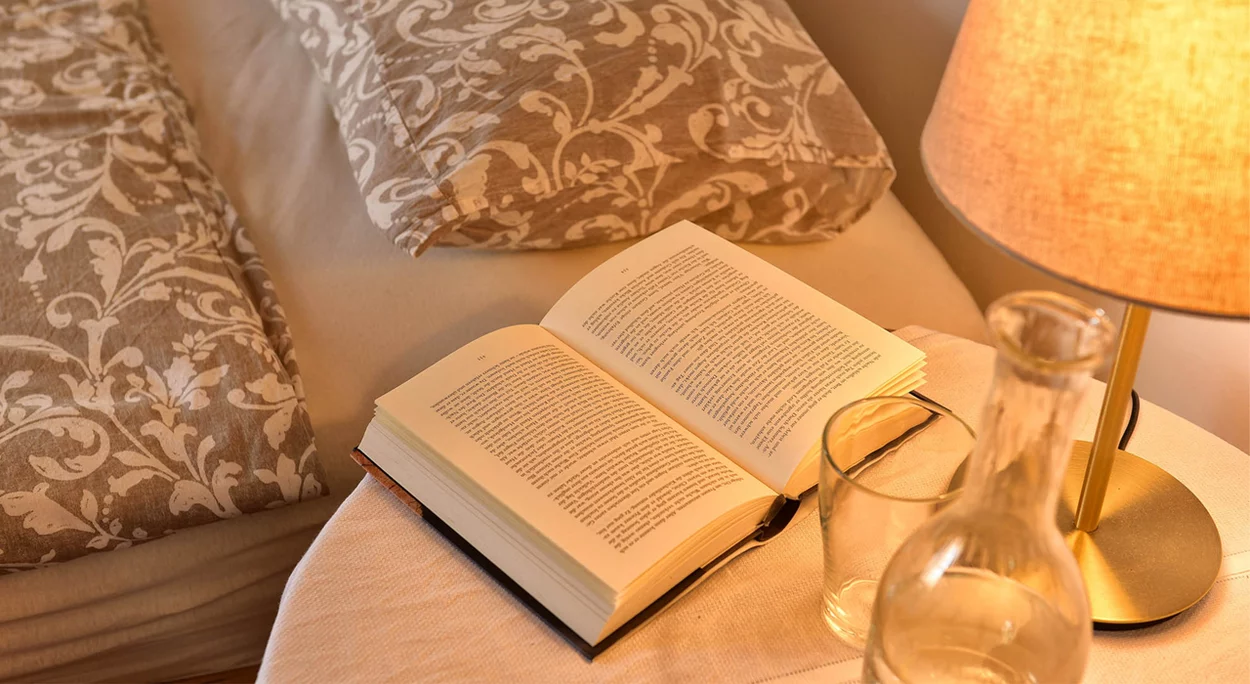 Nachttisch mit Lampe und aufgeschlagenem Buch